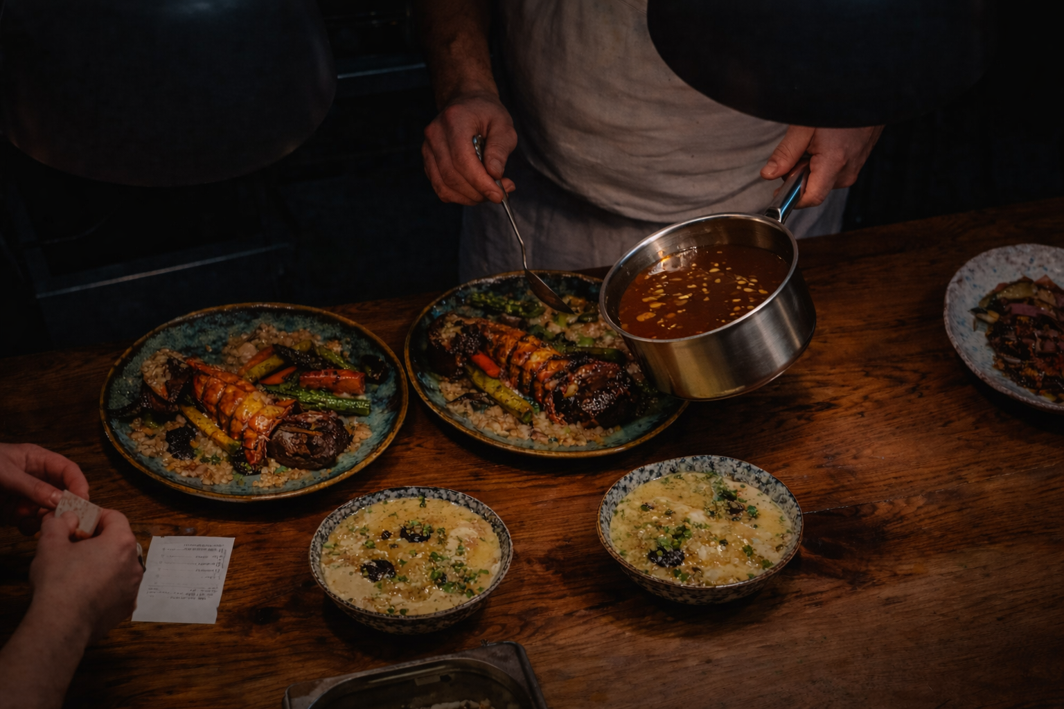 Chef finishing steak and lobster with a glossy brown sauce in a professional kitchen